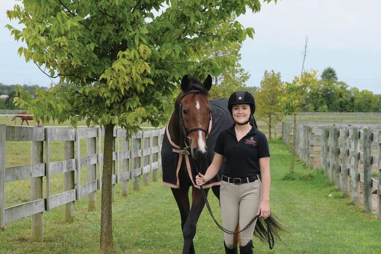 A girl poses with a brown horse.