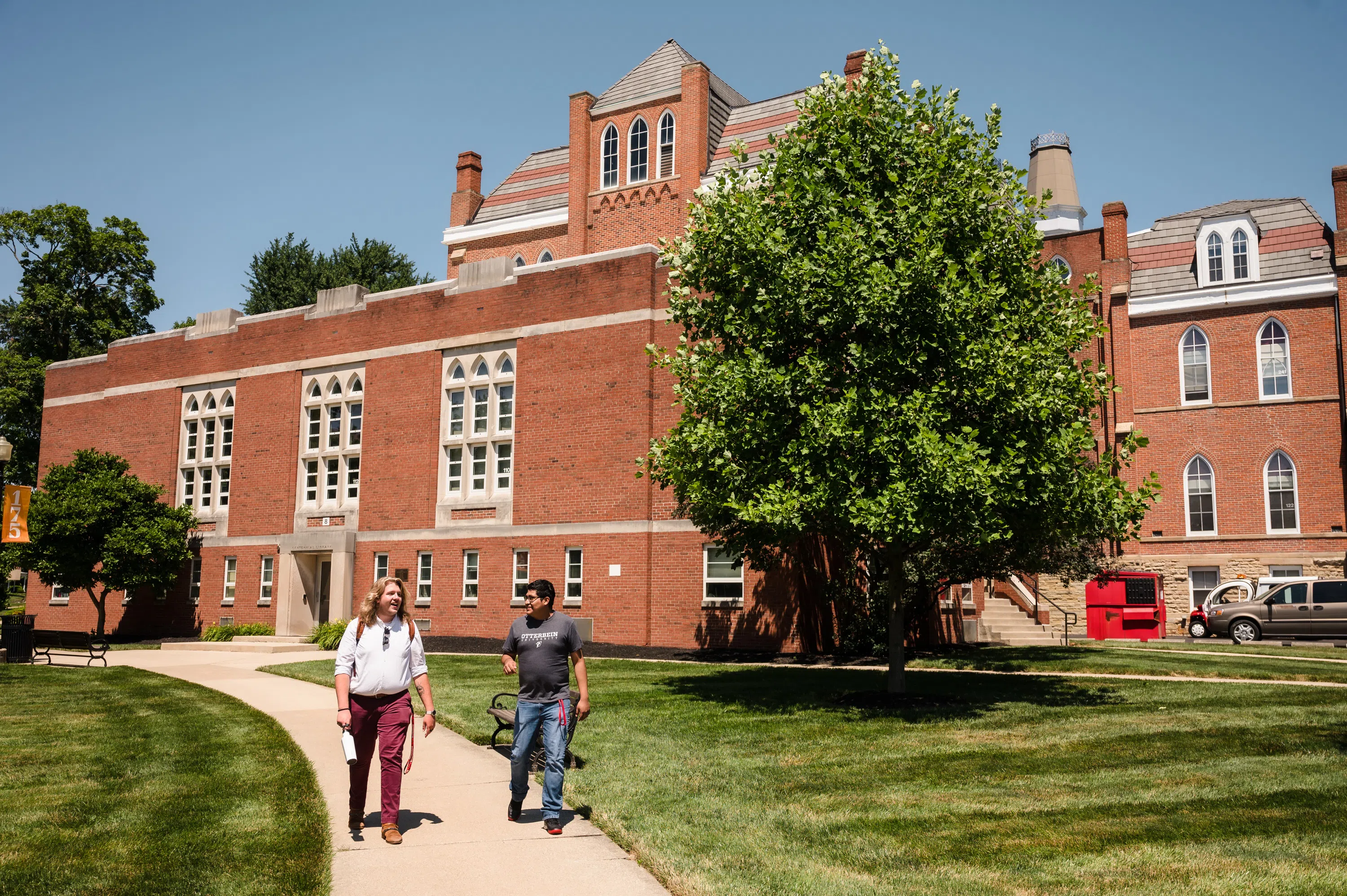 Two students walking in front of an orange brick building (Towers).