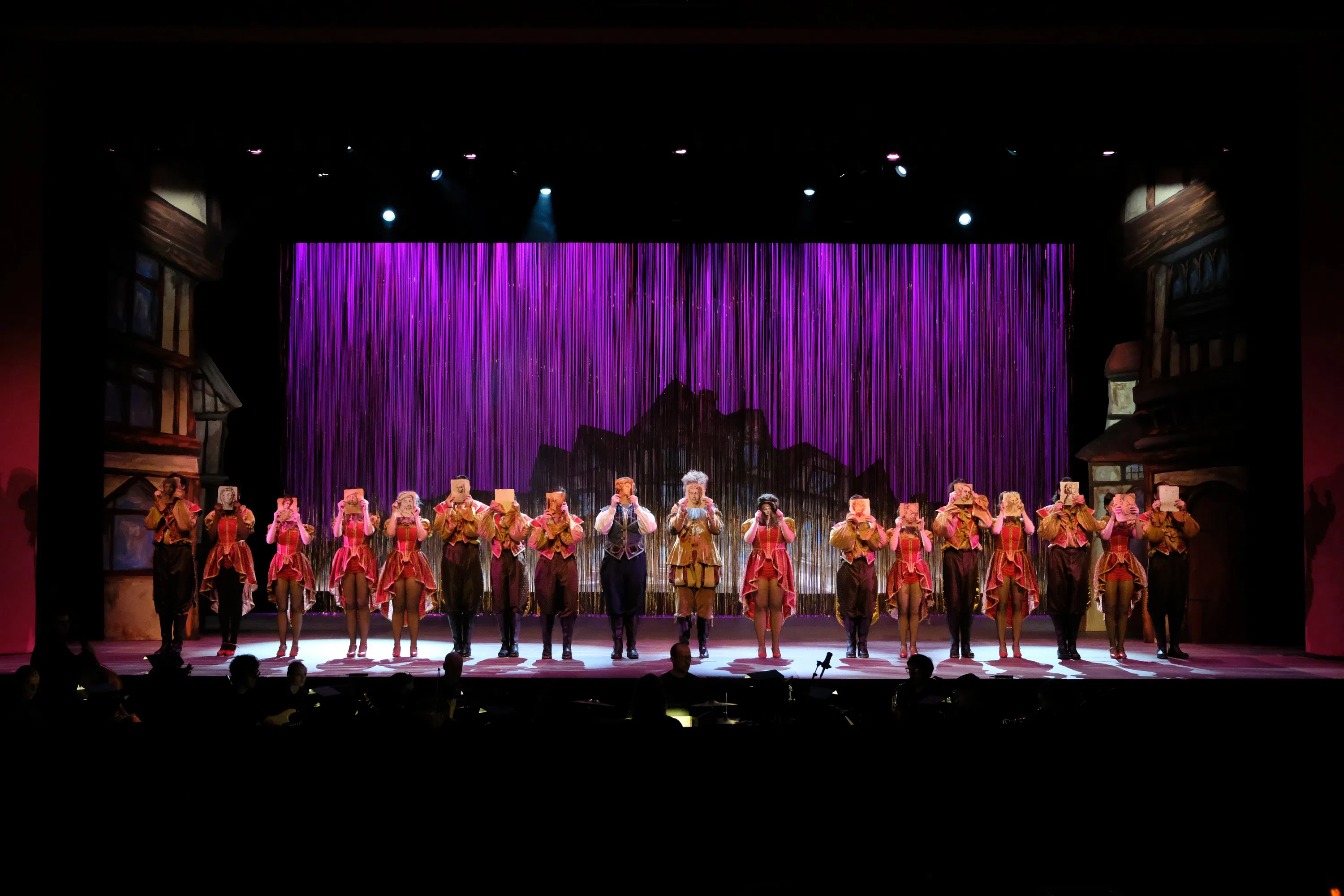 The cast members of a show are lined up at the front of the stage.