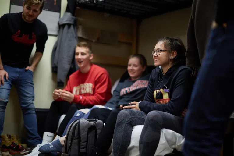 A diverse group of students play video games in a dorm room.