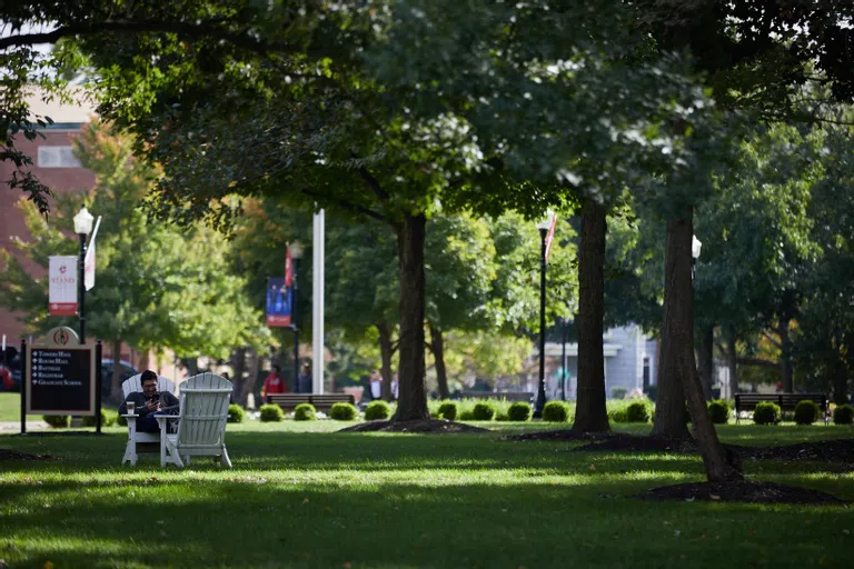 A student sits in one of many adirondack chairs in a green area of campus.