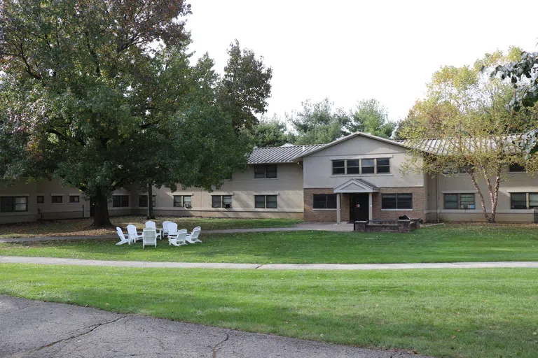 Front view of one of the wings of Mayne Hall. L-shaped two story concrete building with a grassy area in front.