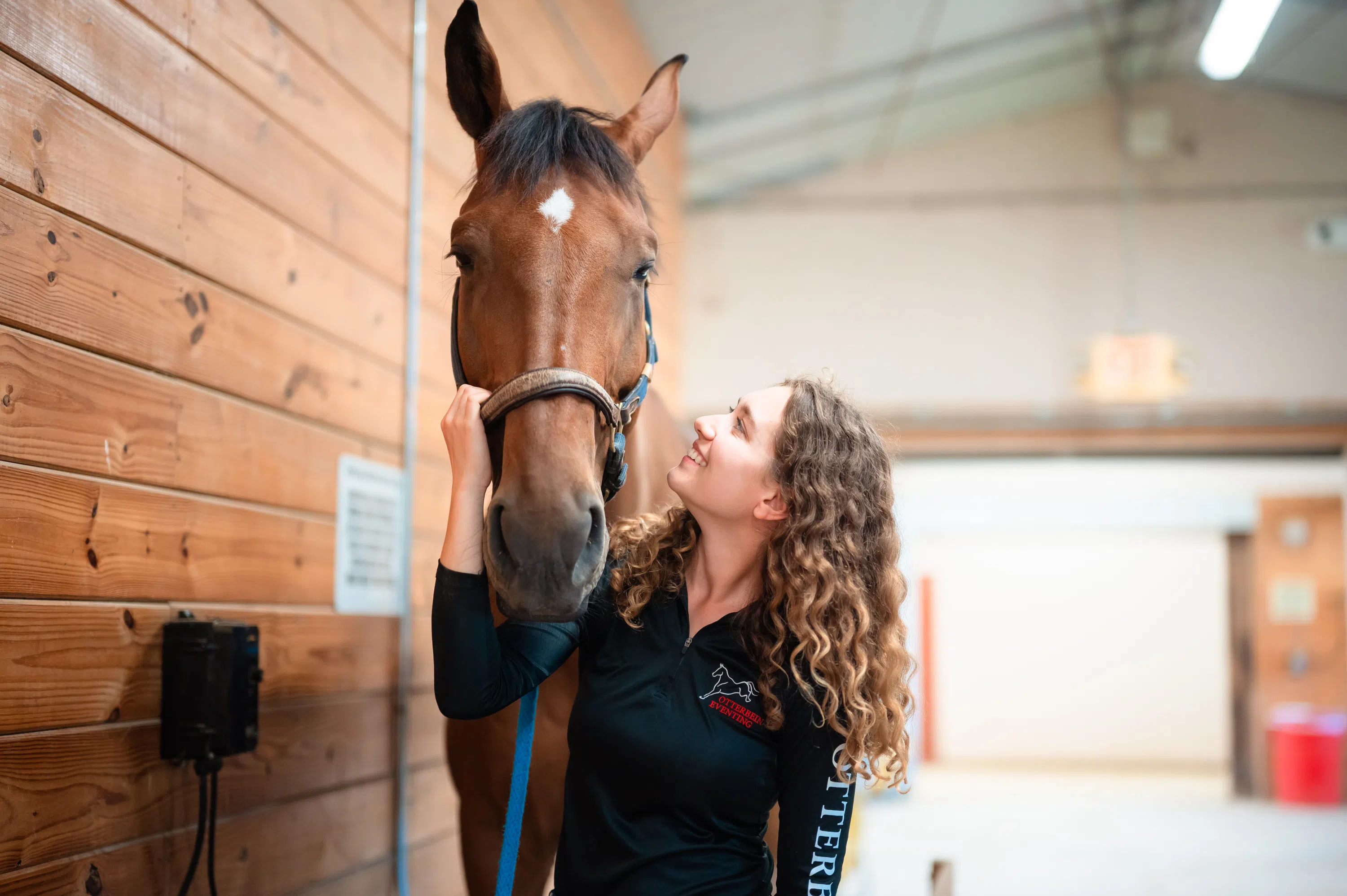 A woman smiles and poses with a brown horse