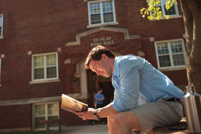 A student sits and reads outside Dunlap King Hall.