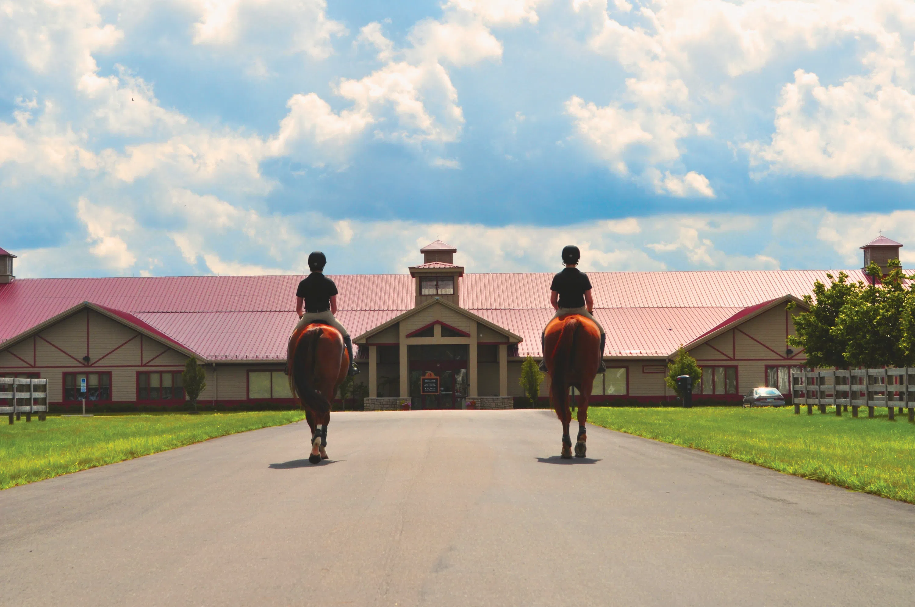 Two people mounted on horses riding towards building