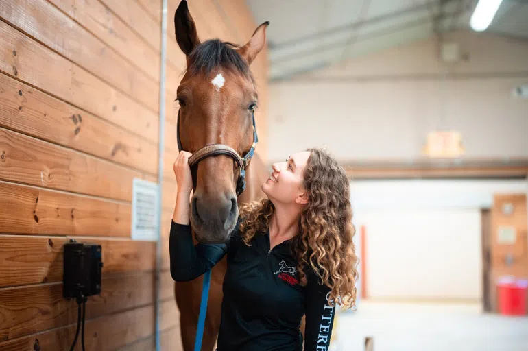 A woman smiles and poses with a brown horse