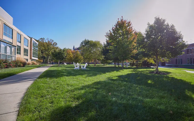 The grounds between the Science Center, Battelle Hall, and Towers Hall. A wide and inviting expanse of lawn with trees criss-crossed by paths and gathering spots with benches and chairs.