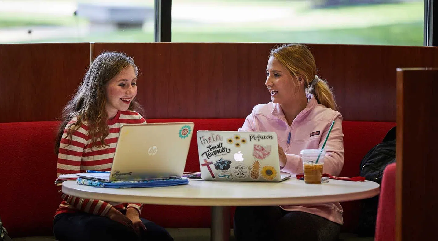 Two students sit together at the round table in the OtterBean, located in the Library Lobby.