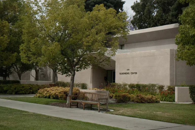 White building with tree and bench in front