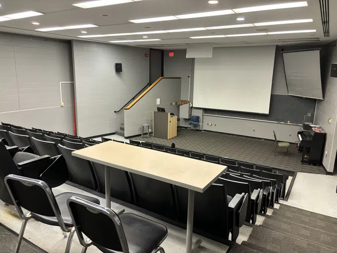 A classroom features a small performance stage.