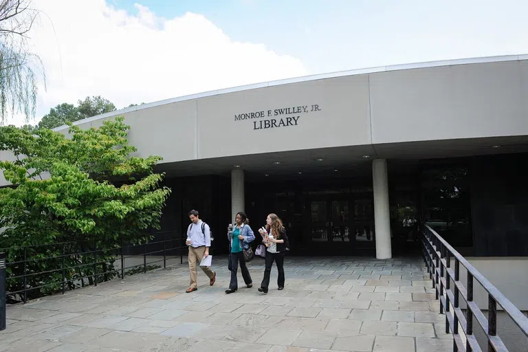 Three students stand near the entrance of the library.