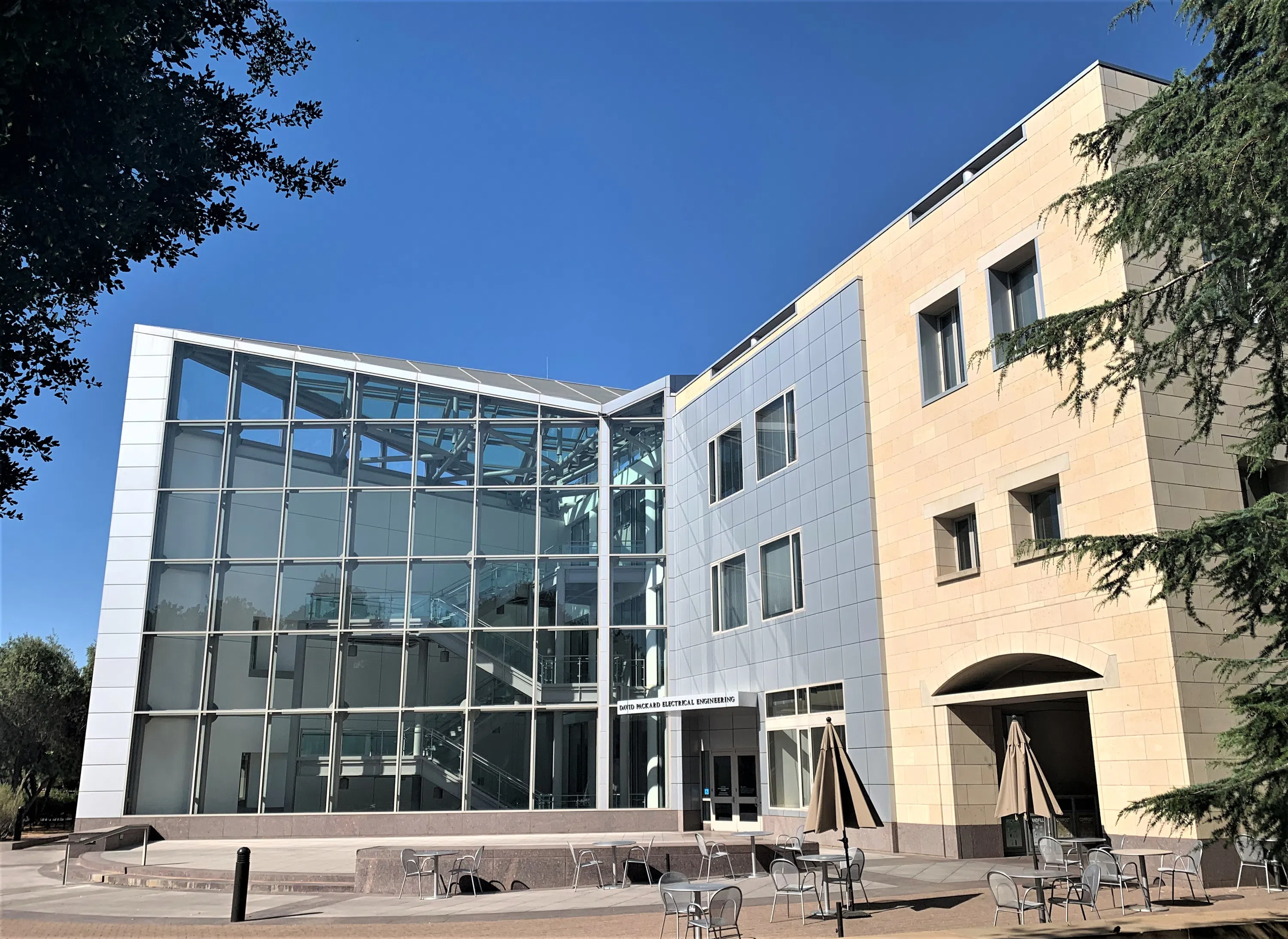 Modern 3-story building with glass front, metallic surfaces, and angled roof on left and a metallic facade on limestone on the right.