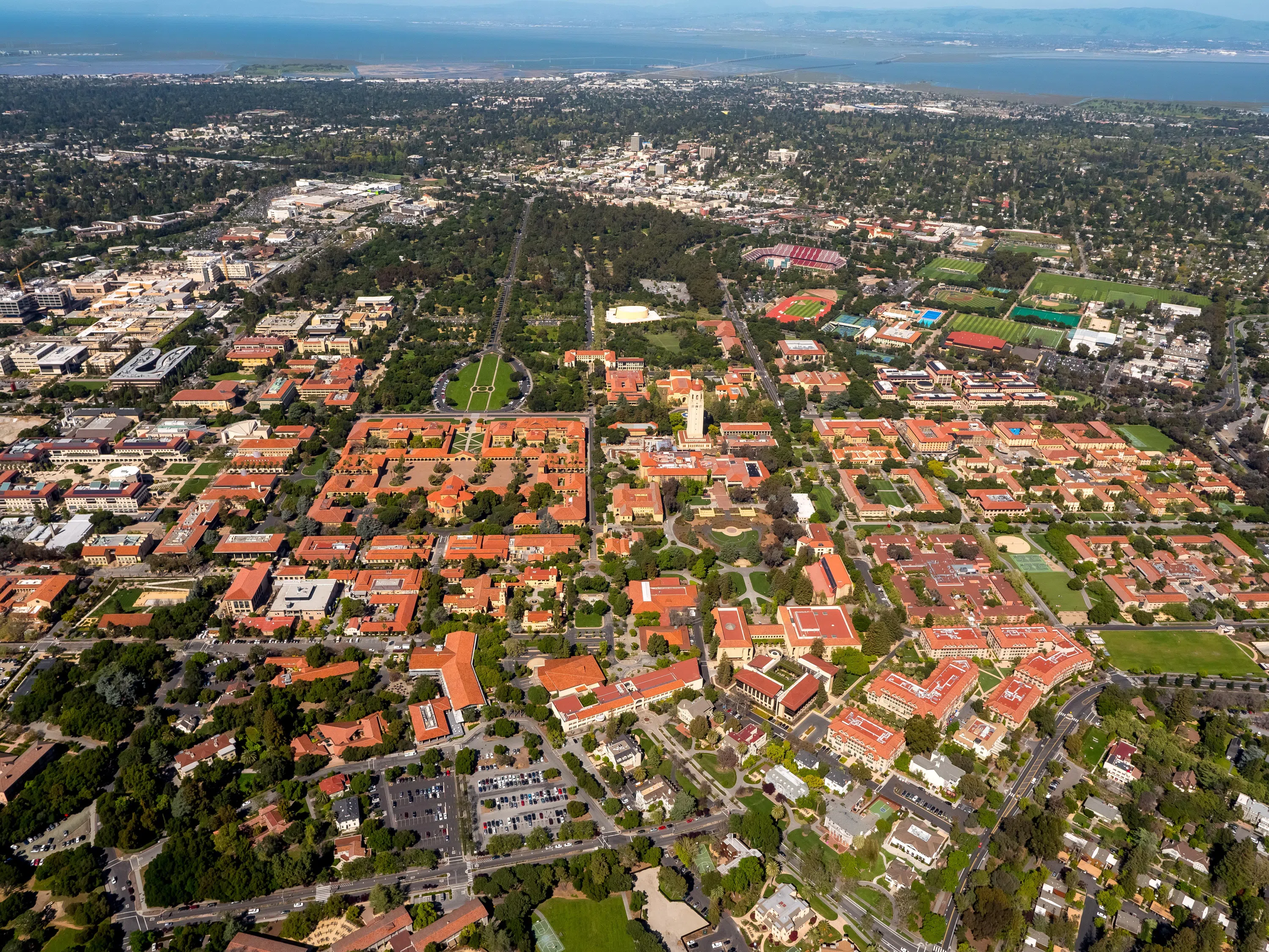 Aerial view of the central campus area of the main Stanford campus, including adjacent communities and San Francisco Bay in background