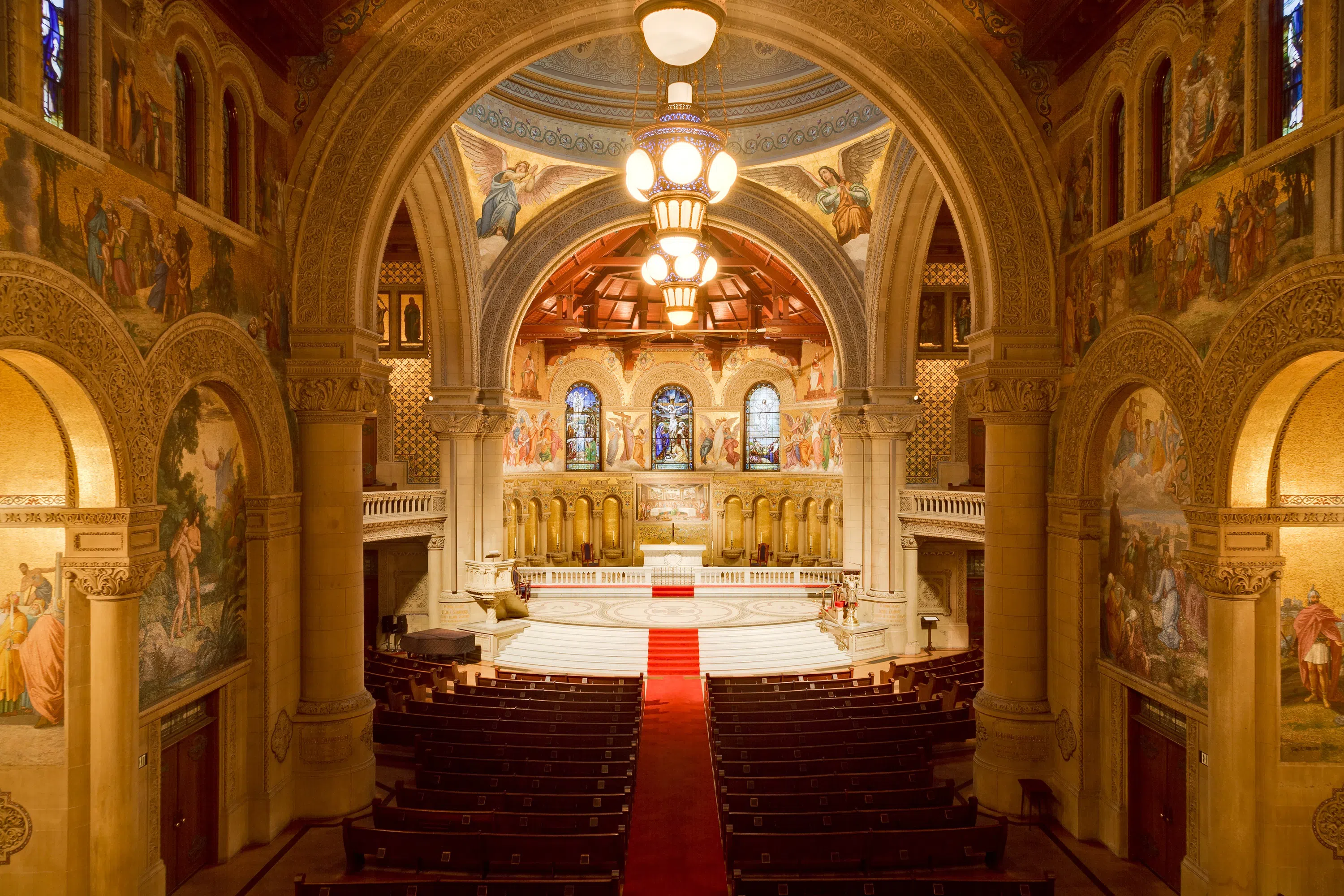 Interior of large cruciform church with elaborate mosaic work, stained glass, and intricately carved sandstone.