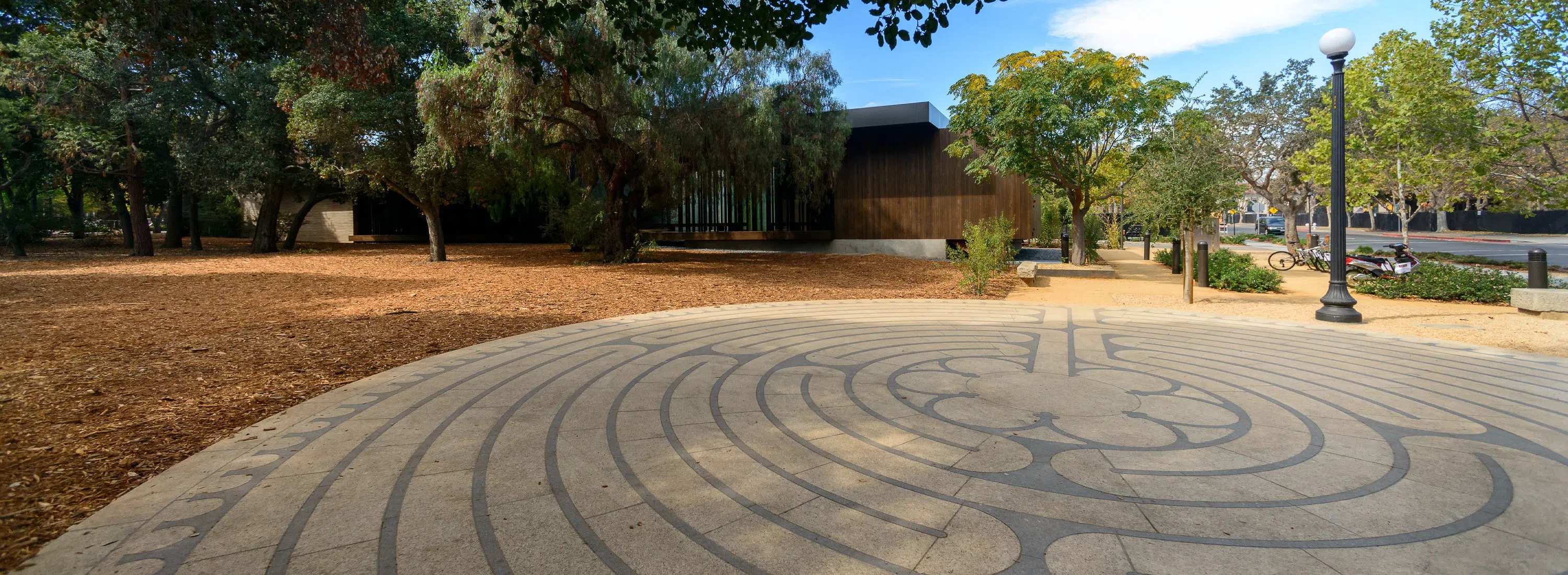 Outdoor walking labyrinth in front of a peaceful facility surrounded by trees.