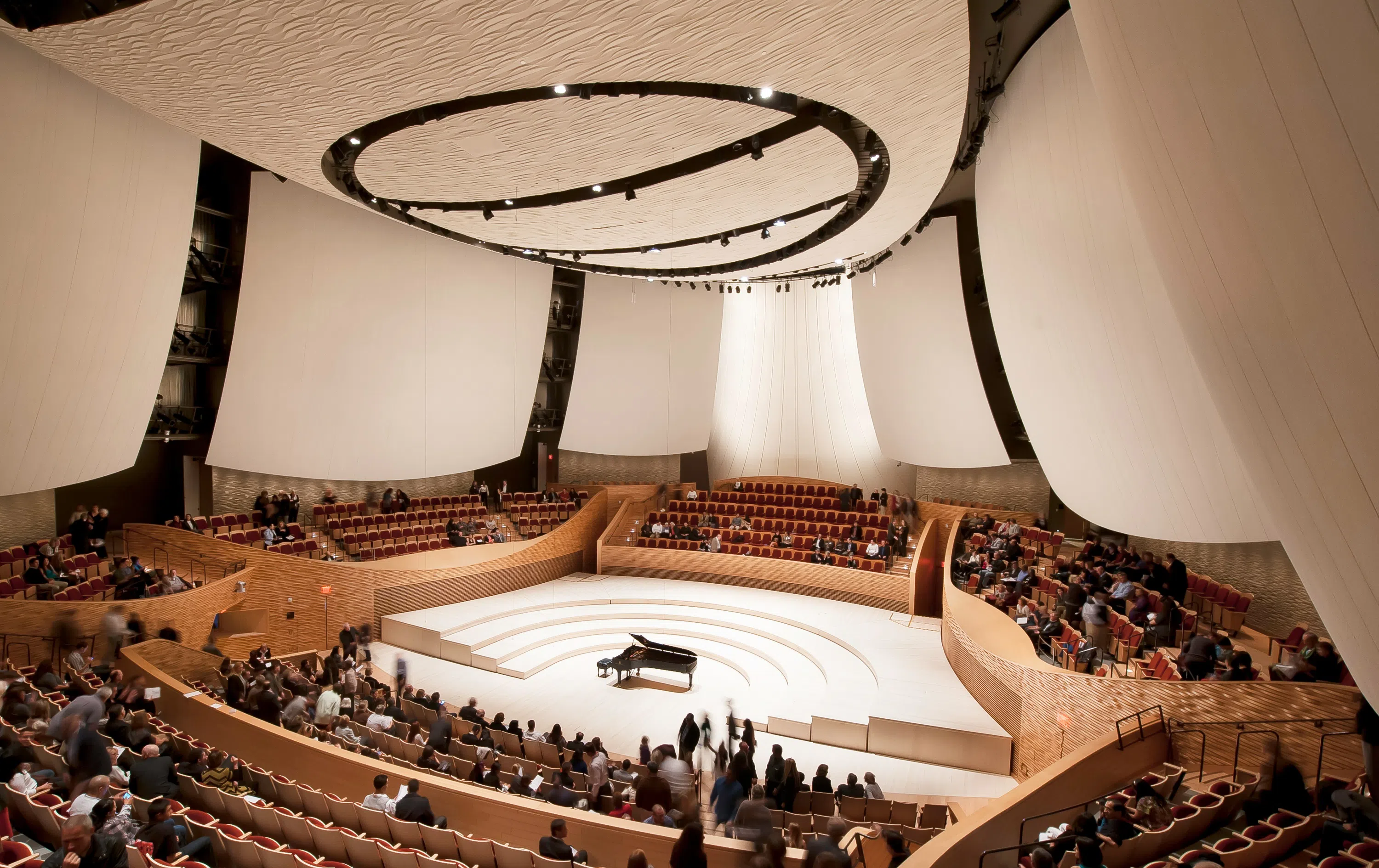 Interior of concert hall with piano set in the middle of a large round seating area beneath several large sound baffles