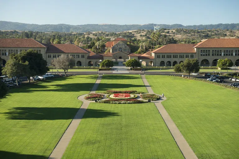 Large oval-shaped lawn area leading up to the sandstone Main Quad and foothills in the background.