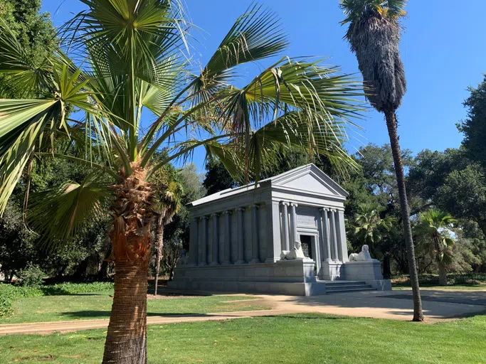 Marble and stone mausoleum with sphinxes at front, surrounded by trees