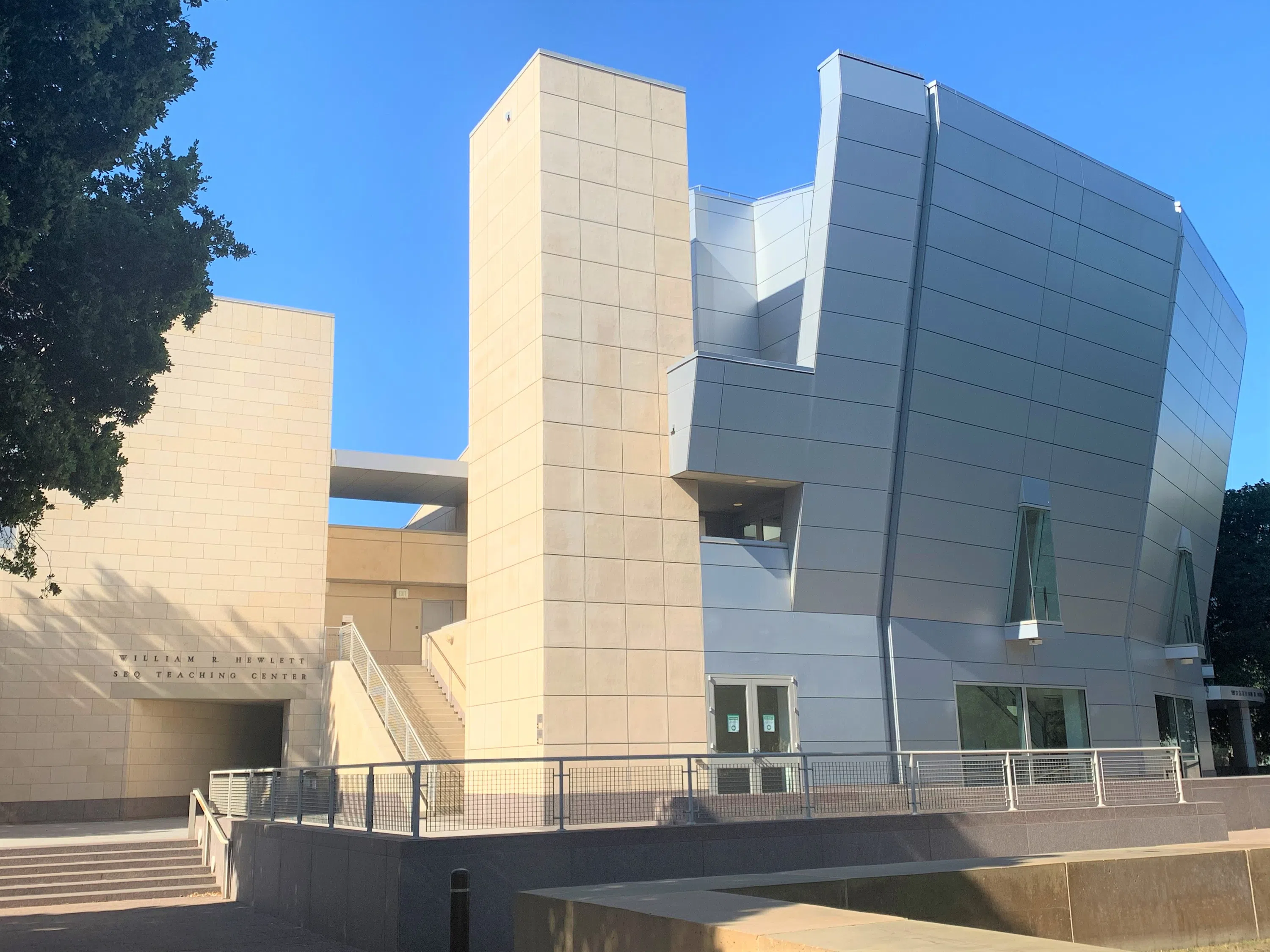 Uniquely shaped auditorium building with sandstone construction on the left, metallic matte finish on the right, and non-traditional roofline.