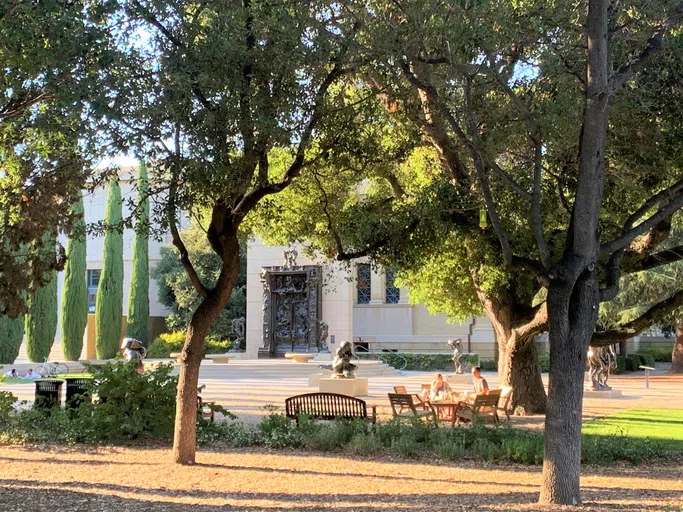 Landscaped garden featuring multiple black bronze sculptures including "The Gates of Hell" outside an adjacent museum