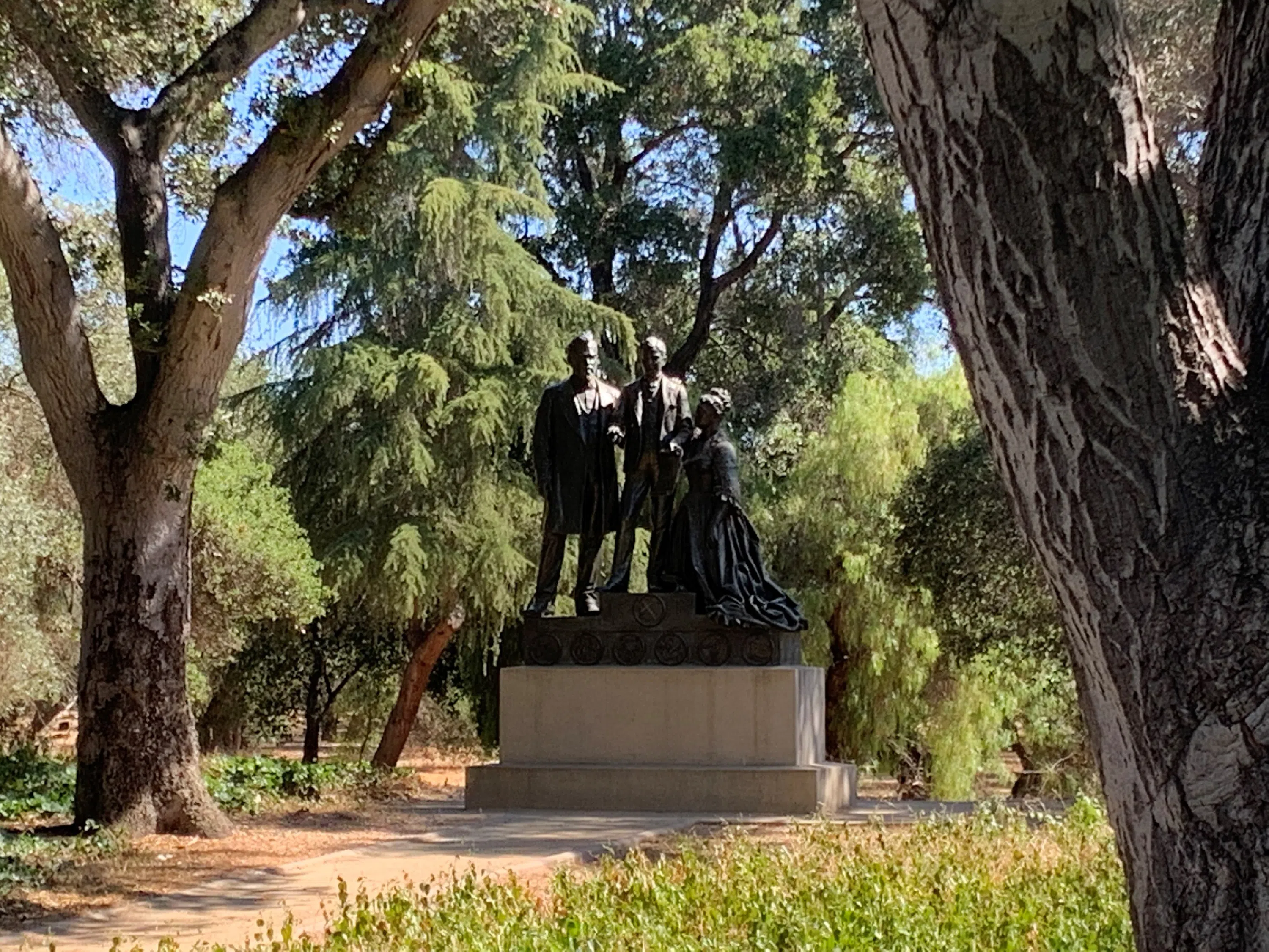 Pedestal containing a bronze statue of the three members of the Stanford family, located amidst trees in the Arboretum
