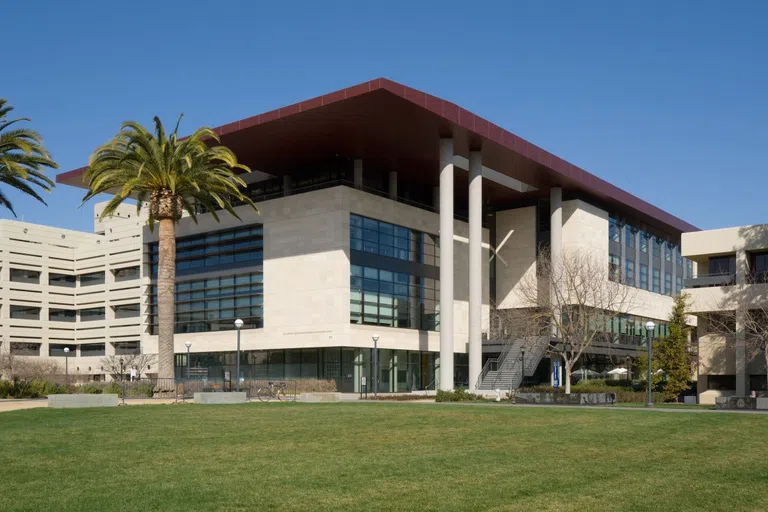 Modern multiple-story medical building with column supports and palm trees an open lawn area in front.