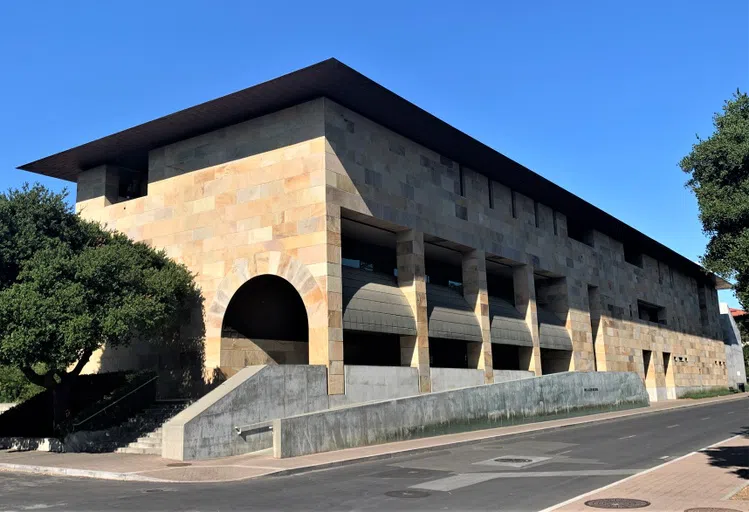 Street view of block-long, 3-story building with modern southwestern stone facade and arched entryway