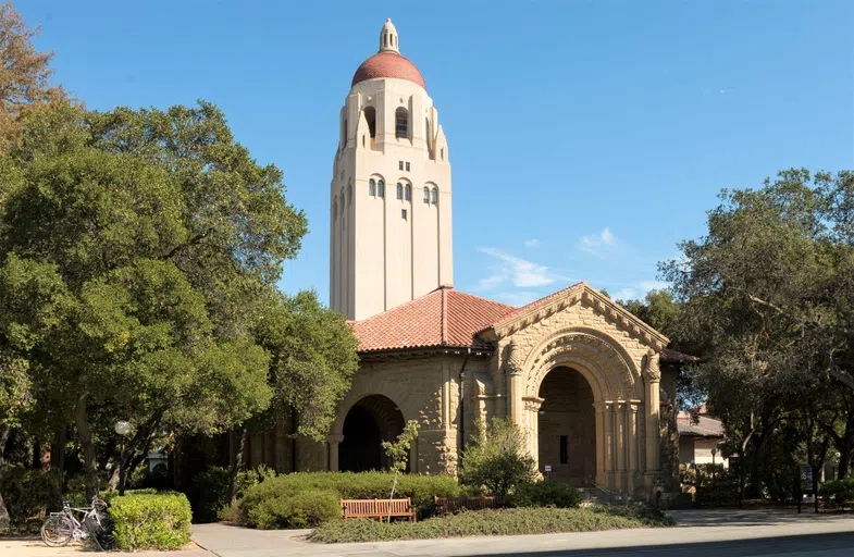 Sandstone gallery building with ornately carved arches, surrounded by trees with Hoover Tower rising up behind it