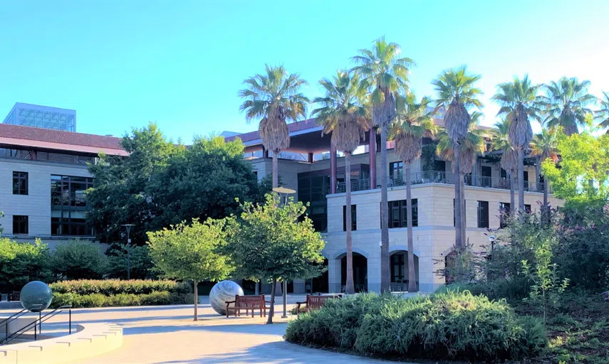 Modern, three-story limestone building, surrounded by palm trees and a courtyard featuring large artistic spheres