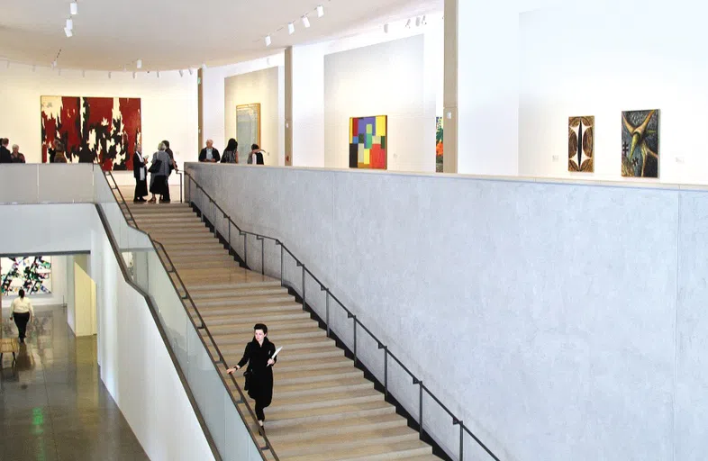 Interior of museum with modern stairwell leading up to second floor gallery displaying modern art paintings