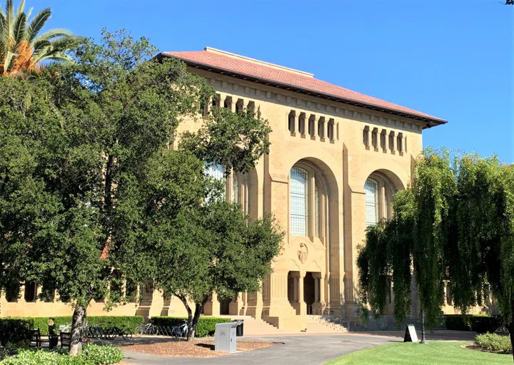 Five-story library building with tall archways, large windows, and trees surrounding trees.