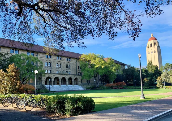 Four-story sandstone building including large front lawn and trees, with Hoover Tower adjacent