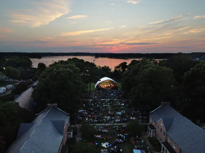 An aerial photo of the Greens during sunset. A shell tent is up for the River Concert and the lawn is covered with concert attendees.