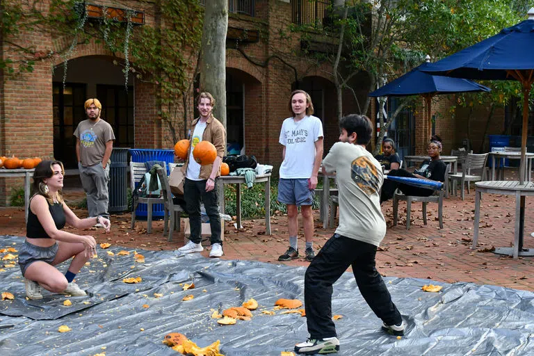 Student mid swing to strike an airborne pumpkin.