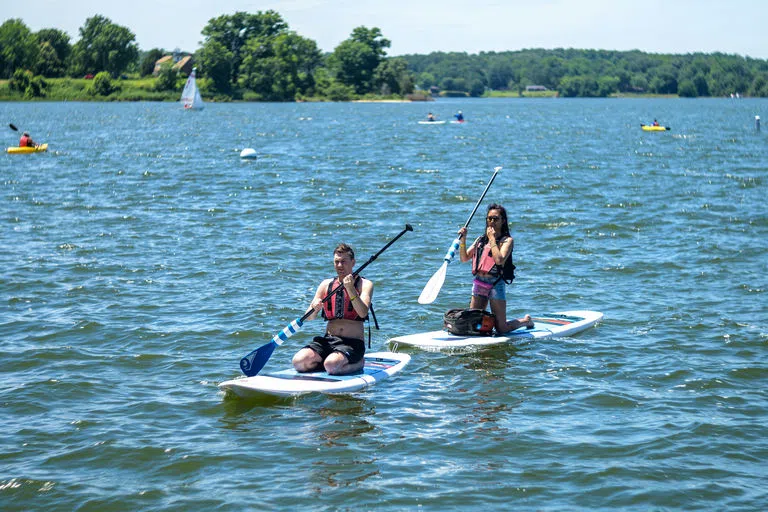 Two people paddle boarding. In the background people can be seen kayaking and sailing.