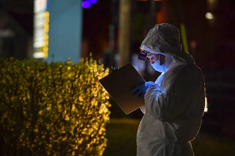 A Forensic Student writes down information on a clipboard outside a Crime Scene House 