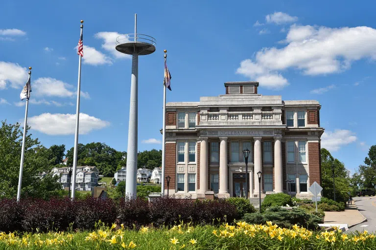 Image shows the front exterior of Oglebay Hall, included the mast of the USS West Virginia installed in the front plaza of the building.