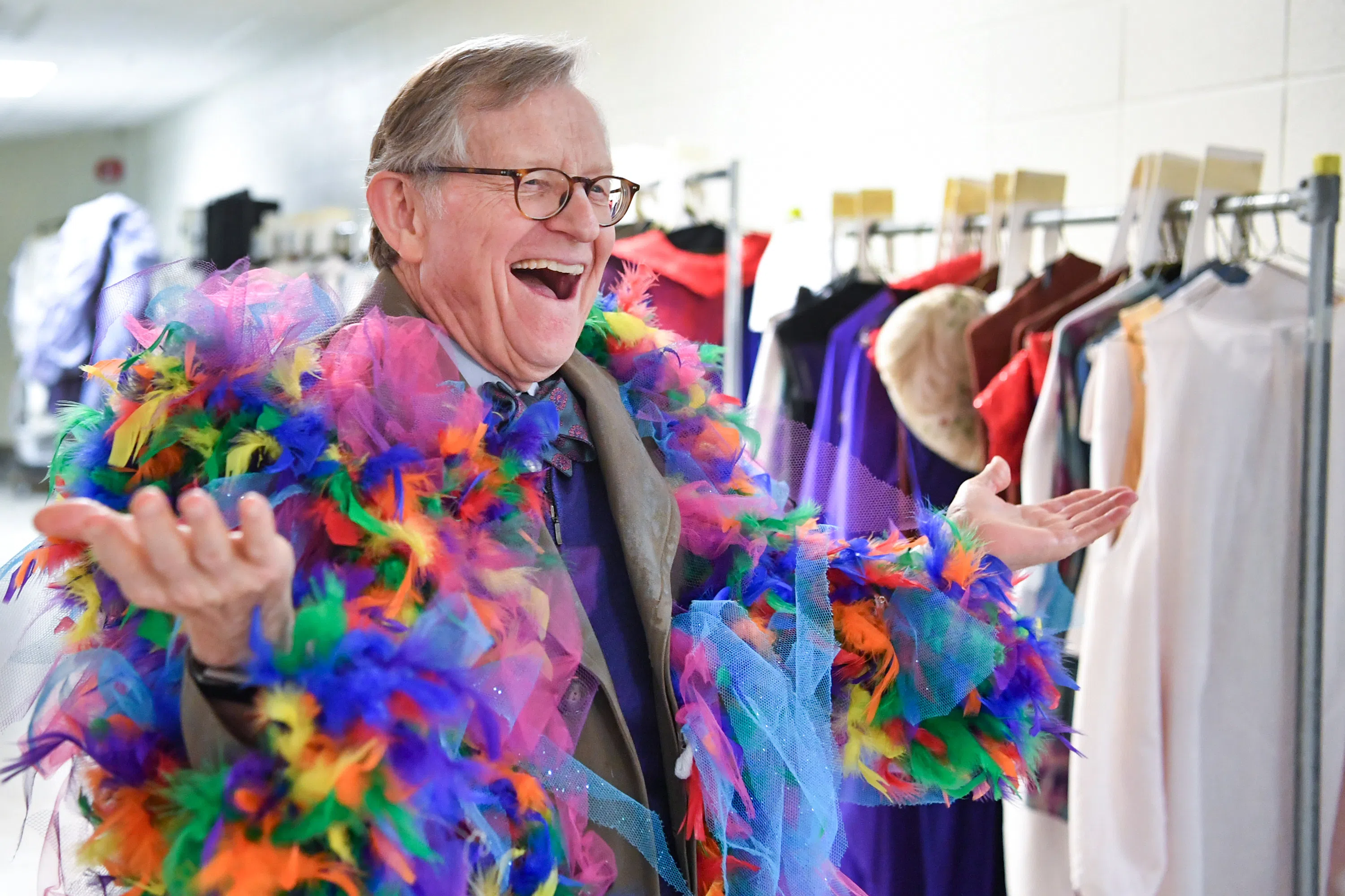 Gordon Gee holds out his arms as he wears a coat covered in rainbow feathers