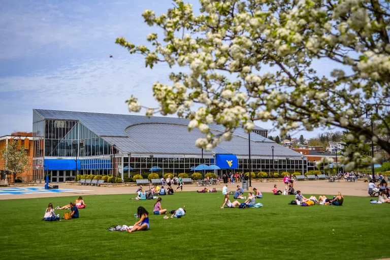 Students are seated outside the Mountainlair student union on the turf area enjoying the sunshine. 