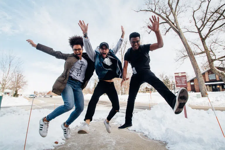 3 students jumping up in the snow happily