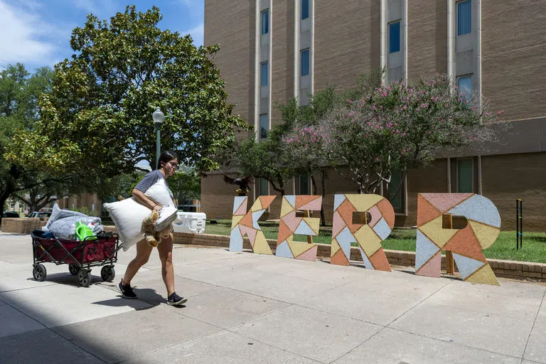 A student carrying personal belongings past the Kerr Hall sign on move-in day.