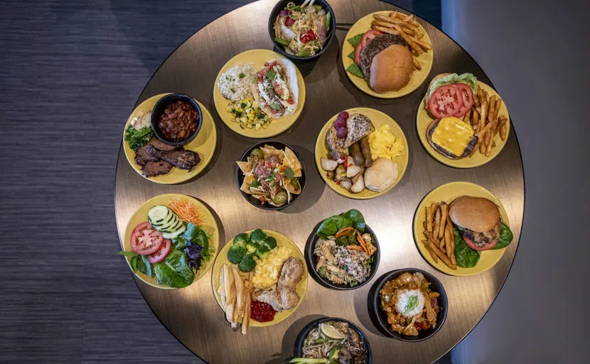 An overhead view of various plates of foods that include burgers and fries, stir fry, salad, and tacos.