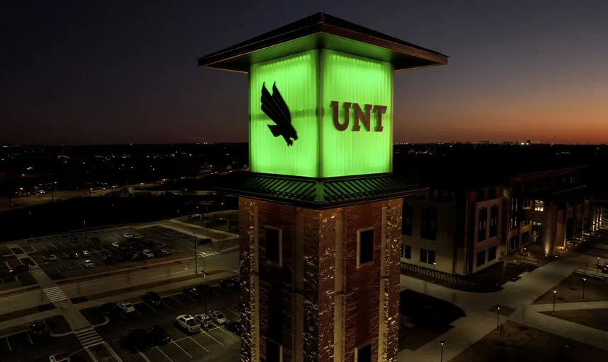 A close up of Frisco Tower lit in green with an aerial view of street and buildings behind it. 