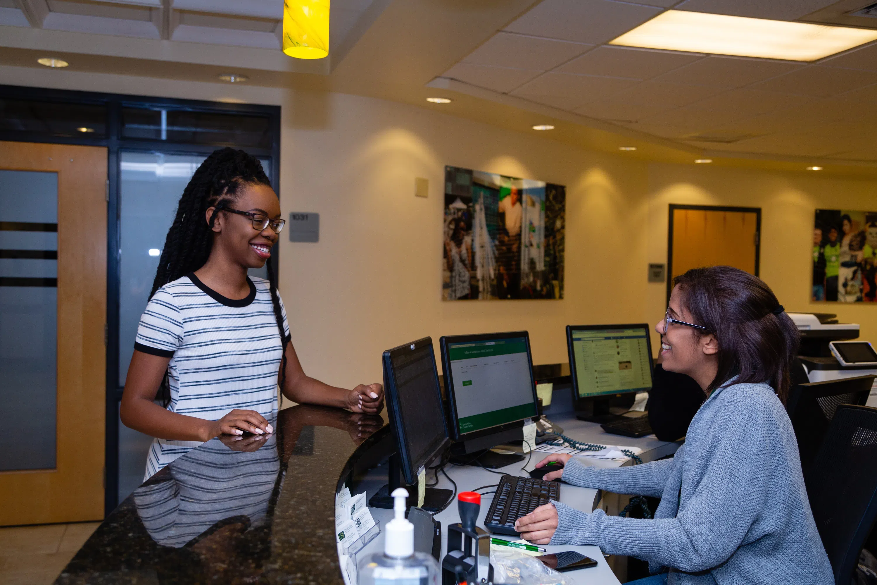 Student (black and white shirt) interacting with an admissions representative (behind the desk).