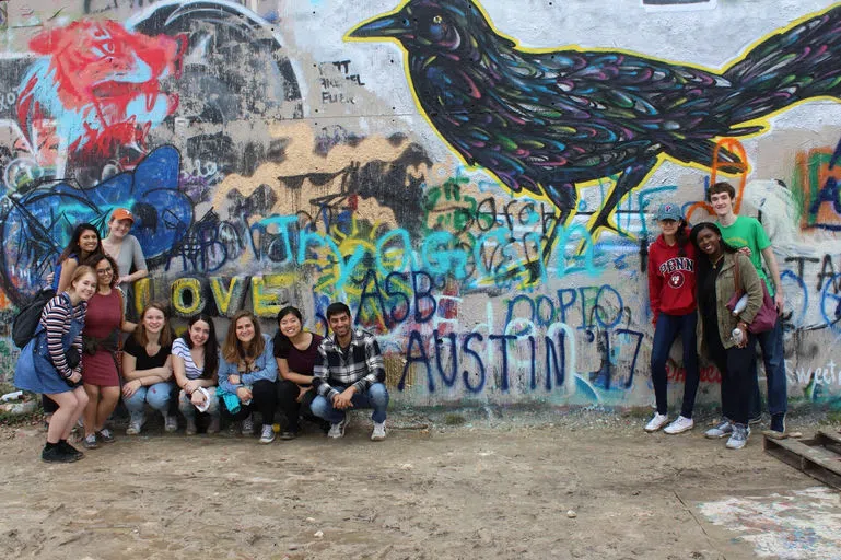 A dozen students pose together in front of a vibrant graffiti wall, with "ASB (Alternative Spring Break): Austin 2017" written on it.