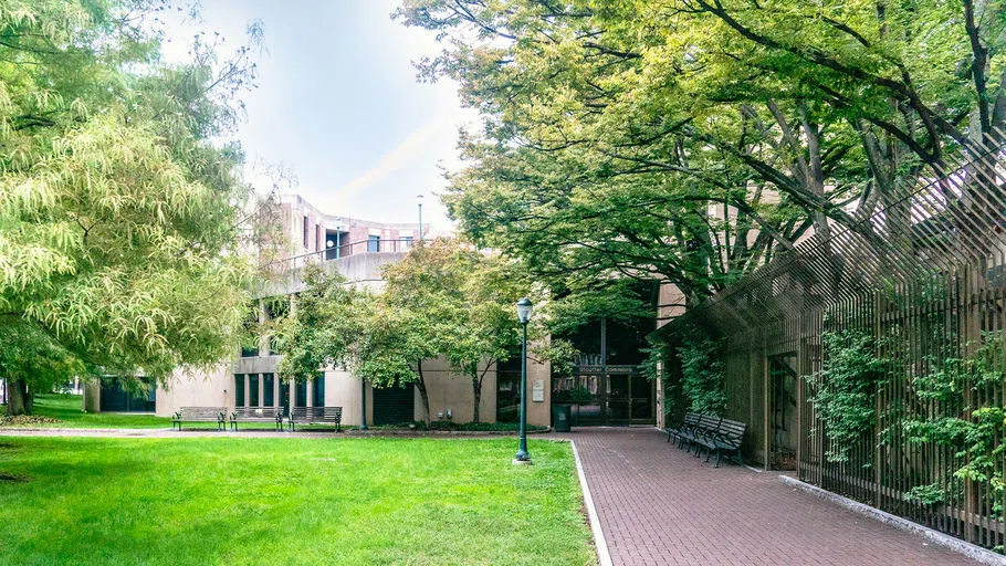 The Weingarten Center's beige building facade nestled in a corner with green space, benches, and trees in the foreground.