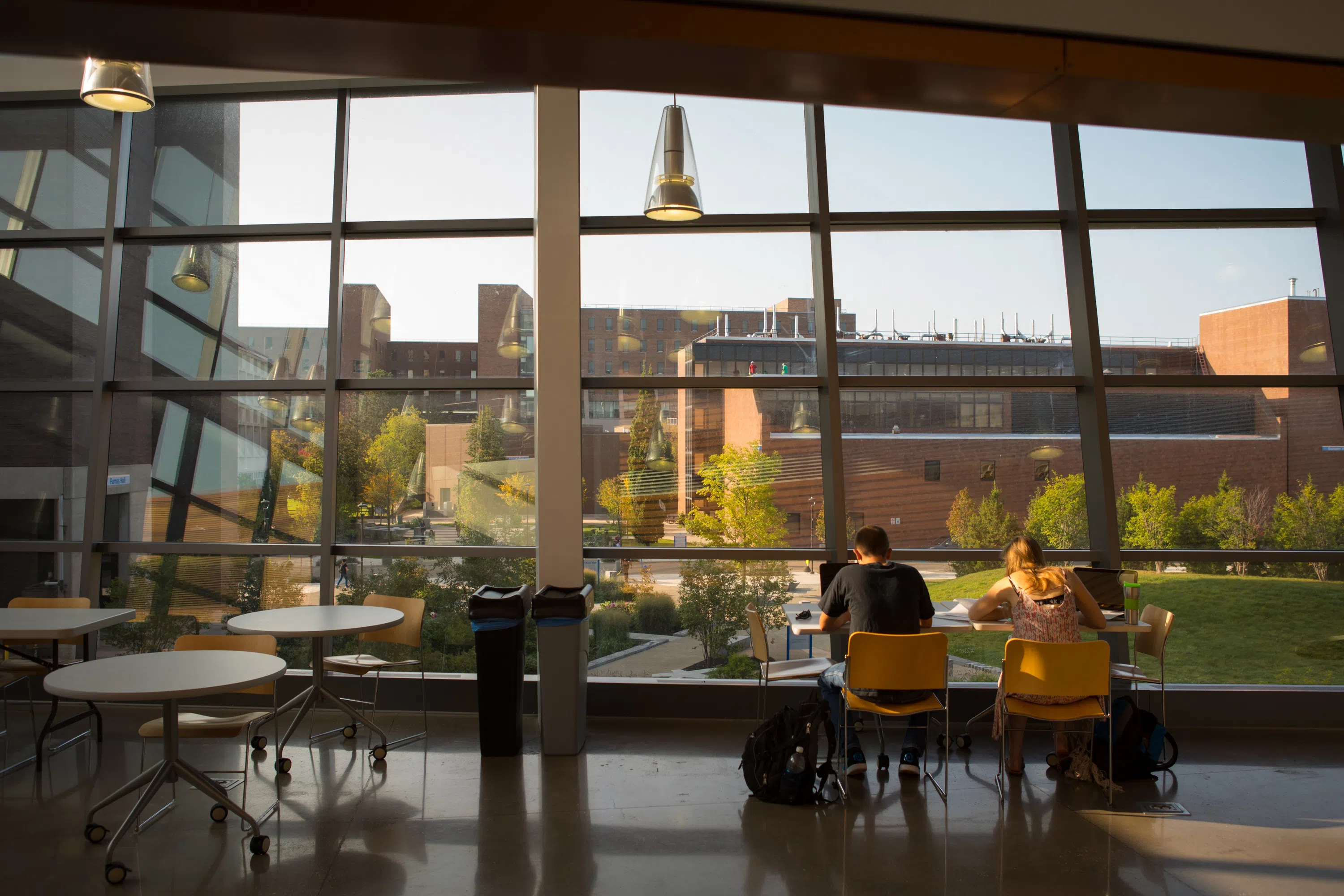 Photo of students sitting at a table looking out a window inside Davis Hall overlooking Grace Plaza.