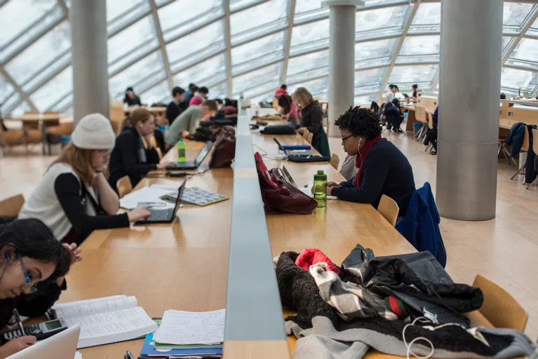 A long table inside a room with a glass ceiling and walls, students are sat there studying