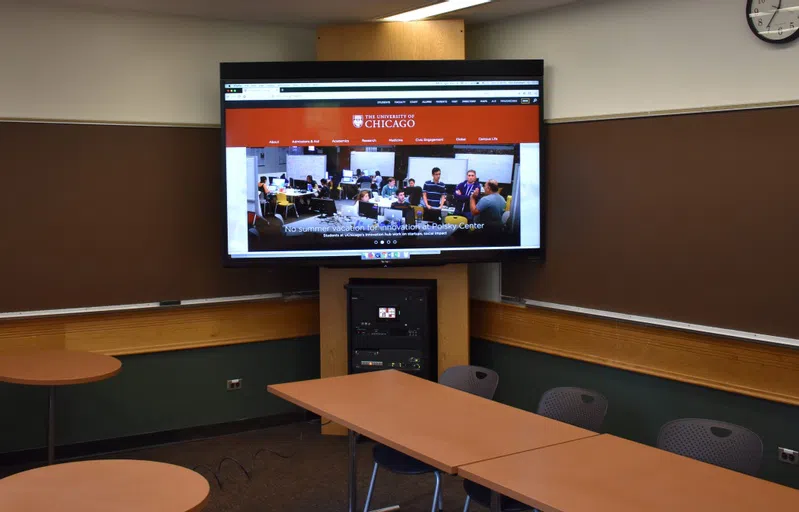 A large TV screen is on in the corner of a classroom