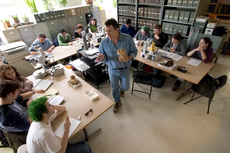 Prof. Paul Serano holds a dinosaur fossil up to students in a classroom